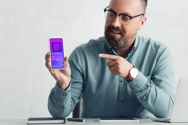 Handsome man in shirt pointing with finger at smartphone with shopping website — Stock Photo