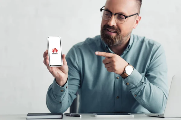 Kyiv, ukraine - 27. August 2019: schöner Geschäftsmann im Hemd, der mit dem Finger auf ein Smartphone mit Huawei-Logo zeigt — Stockfoto