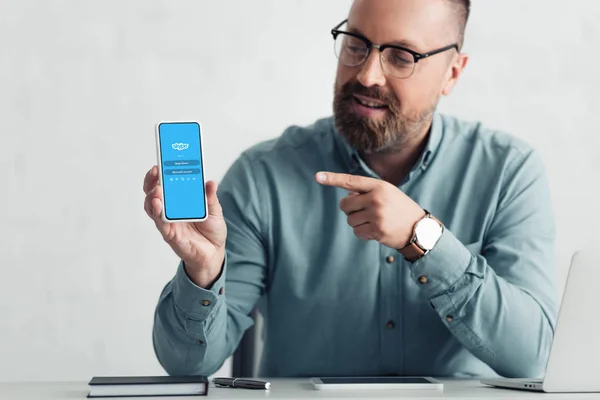 KYIV, UKRAINE - AUGUST 27, 2019: handsome businessman in shirt pointing with finger at smartphone with skype logo — Stock Photo