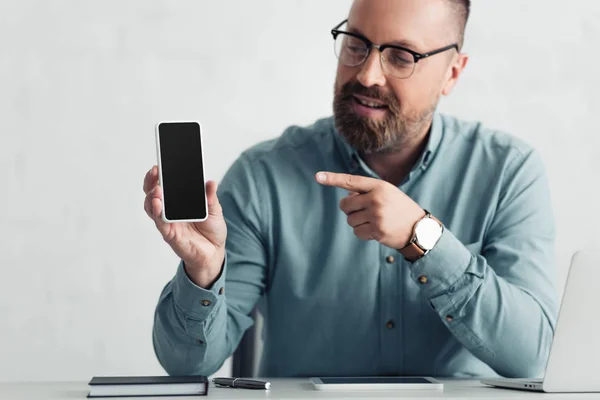 Hombre de negocios guapo en camisa apuntando con el dedo al teléfono inteligente con espacio de copia - foto de stock