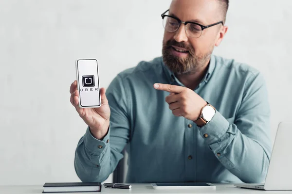 KYIV, UKRAINE - AUGUST 27, 2019: handsome businessman in shirt pointing with finger at smartphone with uber logo — Stock Photo