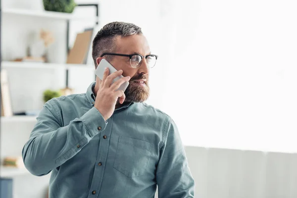 Hombre de negocios guapo en camisa hablando en smartphone y mirando hacia otro lado - foto de stock