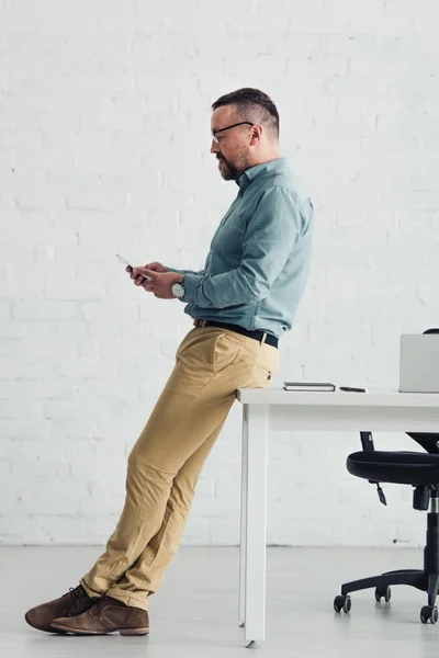 Vue latérale du bel homme d'affaires en chemise tenant smartphone — Photo de stock