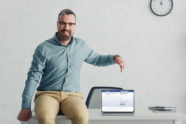 Kyiv, ukraine - 27. August 2019: gutaussehender Geschäftsmann im Hemd, der mit dem Finger auf Laptop mit Facebook-Seite zeigt — Stockfoto