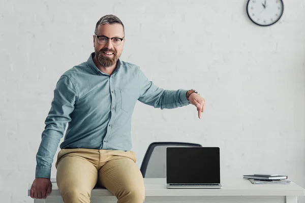 Schöner Geschäftsmann sitzt am Tisch und zeigt mit dem Finger auf Laptop mit Kopierplatz — Stockfoto