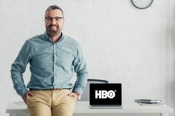 KYIV, UKRAINE - AUGUST 27, 2019: handsome businessman sitting on table near laptop with hbo logo — Stock Photo