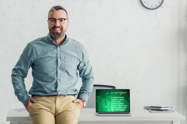 Schöner Geschäftsmann sitzt auf einem Tisch neben Laptop mit Gesundheits-Website — Stockfoto