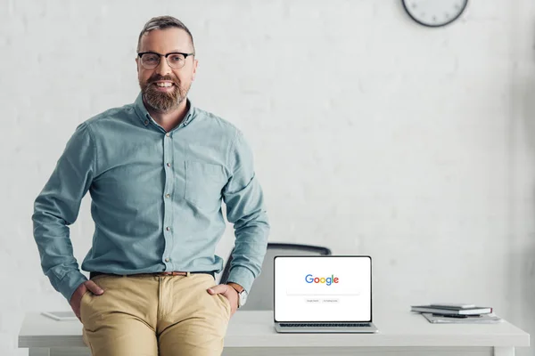 KYIV, UKRAINE - 27 de agosto de 2019: belo homem de negócios sentado na mesa perto do laptop com o logotipo do google — Fotografia de Stock