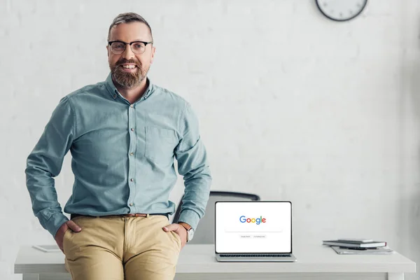 Kyiv, ukraine - 27. August 2019: gutaussehender Geschäftsmann sitzt auf einem Tisch neben Laptop mit Google-Logo — Stockfoto