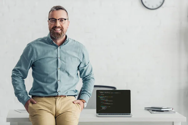 KYIV, UCRANIA - 27 de agosto de 2019: hombre de negocios guapo sentado en la mesa cerca de la computadora portátil con sitio web - foto de stock