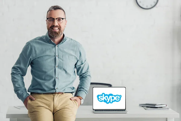 KYIV, UKRAINE - AUGUST 27, 2019: handsome businessman sitting on table near laptop with skype logo — Stock Photo