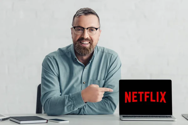 KYIV, UCRANIA - 27 de agosto de 2019: hombre de negocios guapo con camisa que señala con el dedo al ordenador portátil con el logotipo de netflix - foto de stock