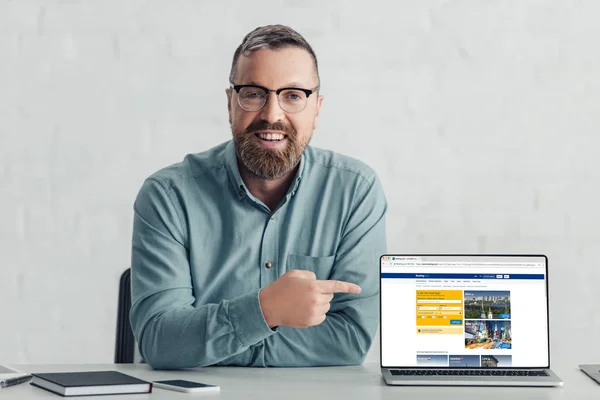 KYIV, UKRAINE - 27 de agosto de 2019: belo homem de negócios de camisa apontando com o dedo para o laptop com site de reserva — Fotografia de Stock