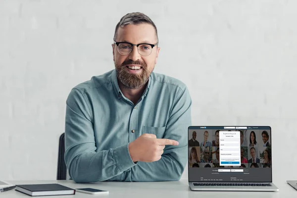 KYIV, UKRAINE - 27 AOÛT 2019 : bel homme d'affaires en chemise pointant du doigt sur un ordinateur portable avec un site Web linkedin — Photo de stock