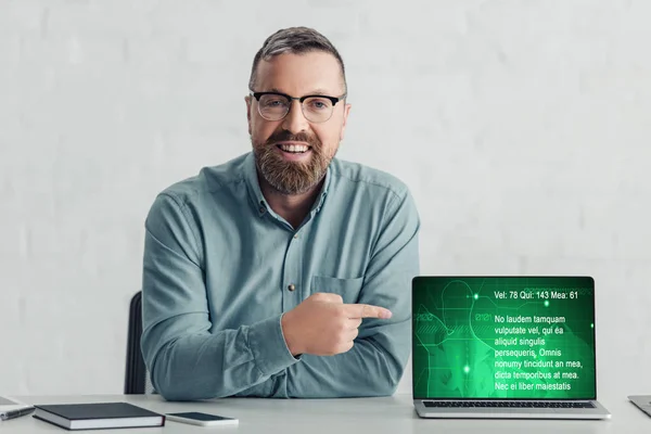 Schöner Geschäftsmann im Hemd zeigt mit dem Finger auf Laptop mit Gesundheits-Website — Stockfoto