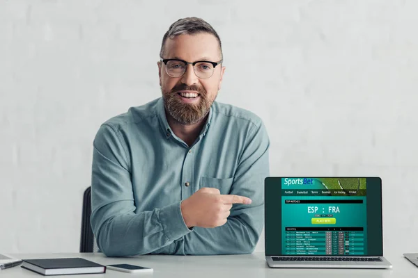 Handsome businessman in shirt pointing with finger at laptop with sports bet website — Stock Photo