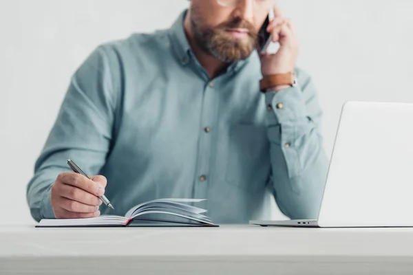 Recortado vista de hombre de negocios en camisa hablando en el teléfono inteligente y la celebración de la pluma - foto de stock