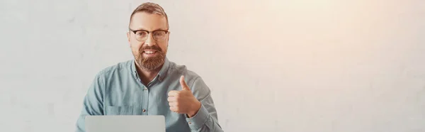 Panoramic shot of handsome businessman in shirt and glasses looking at camera and showing thumb up — Stock Photo