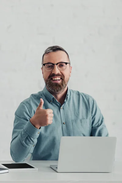 Guapo hombre de negocios en camisa y gafas mirando a la cámara y mostrando el pulgar hacia arriba - foto de stock