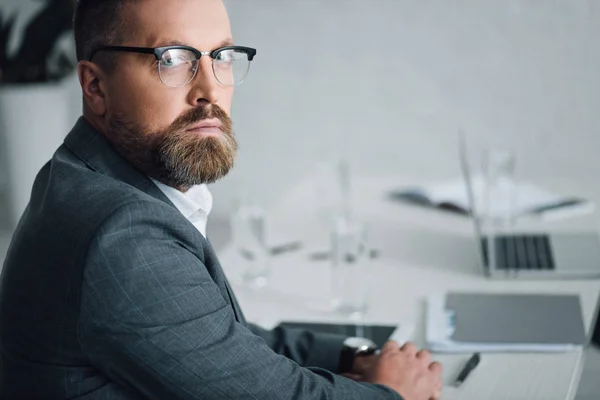 Красивий бізнесмен у формальному одязі та окулярах дивиться на камеру в офісі — стокове фото