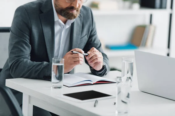 Cropped view of businessman in formal wear holding pen in office — Stock Photo