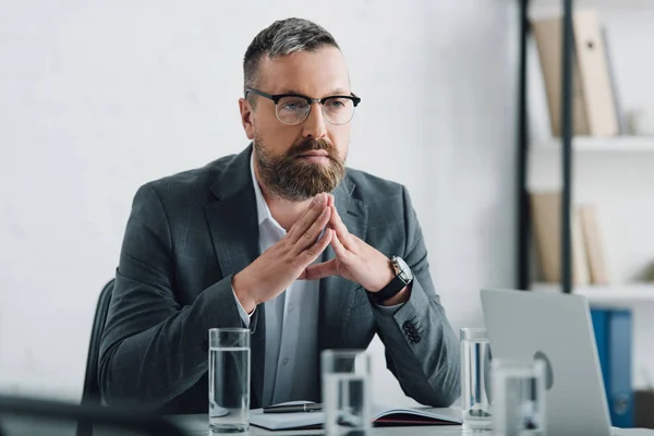 Guapo hombre de negocios en ropa formal y gafas mirando hacia otro lado en la oficina - foto de stock