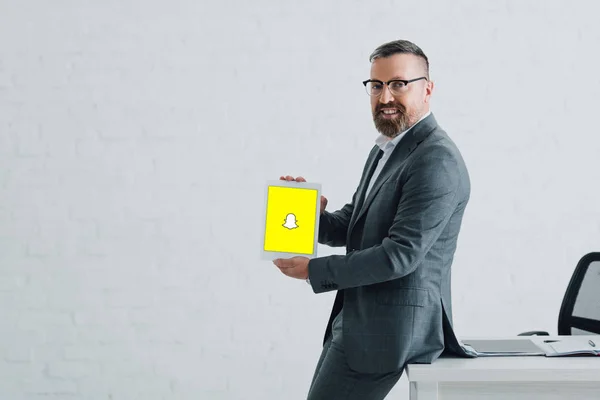KYIV, UKRAINE - 27 de agosto de 2019: belo homem de negócios em uso formal segurando tablet digital com logotipo Snapchat — Fotografia de Stock