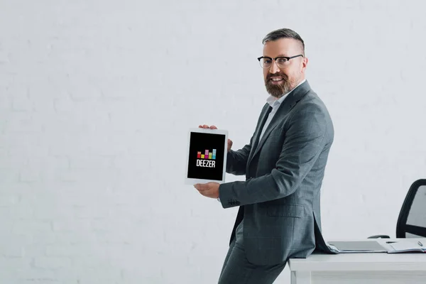 KYIV, UKRAINE - 27 AOÛT 2019 : bel homme d'affaires en tenue formelle tenant tablette numérique avec logo deezer — Photo de stock