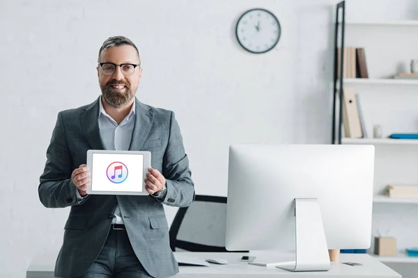 KYIV, UKRAINE - AUGUST 27, 2019: handsome businessman in formal wear holding digital tablet with apple music logo — Stock Photo