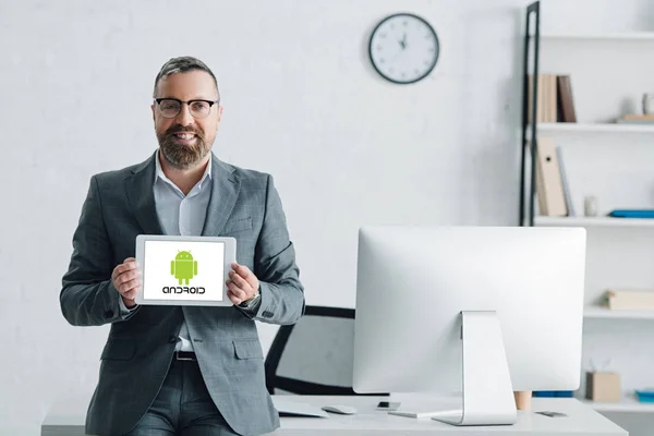 KYIV, UKRAINE - AUGUST 27, 2019: handsome businessman in formal wear holding digital tablet with android logo — Stock Photo