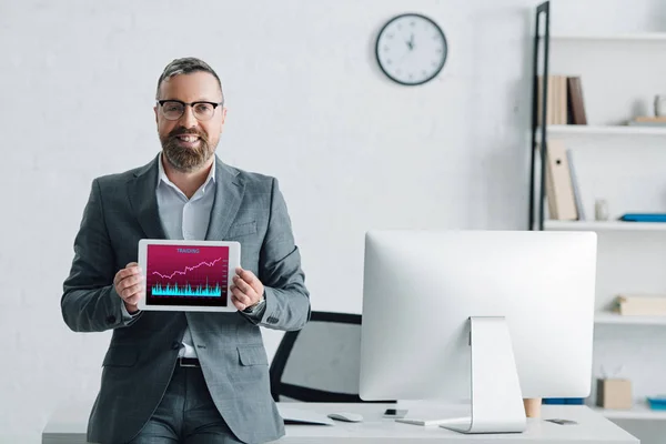 Красивий бізнесмен у формальному носінні тримає цифровий планшет з графами на екрані — стокове фото