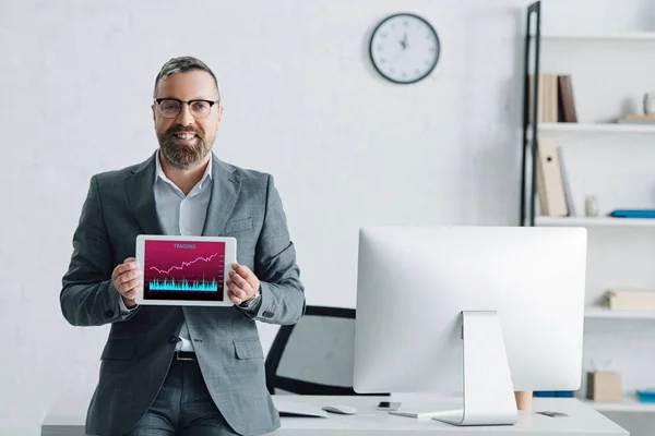 Handsome businessman in formal wear holding digital tablet with graphs on screen — Stock Photo