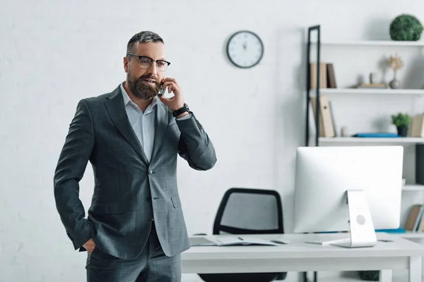 Hombre de negocios guapo en ropa formal y gafas hablando en el teléfono inteligente - foto de stock