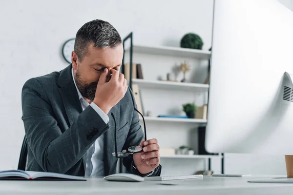 Uomo d'affari barbuto in abbigliamento formale che tiene gli occhiali in ufficio — Foto stock