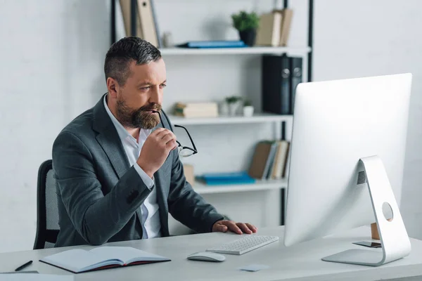 Bonito empresário no formal desgaste segurando óculos e olhando para o computador — Fotografia de Stock