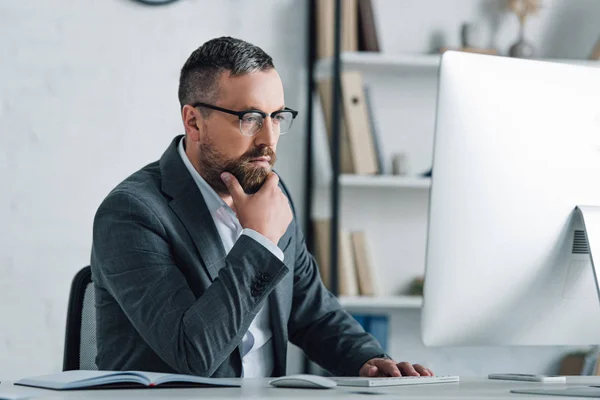 Guapo hombre de negocios en ropa formal y gafas mirando a la computadora - foto de stock