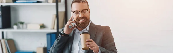 Panoramic shot of businessman in formal wear talking on smartphone and holding paper cup — Stock Photo
