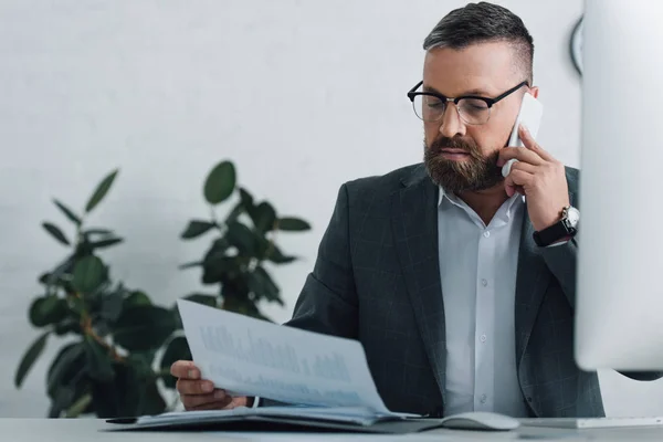 Handsome businessman in formal wear talking on smartphone and holding document — Stock Photo