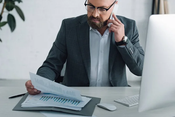 Hombre de negocios guapo en ropa formal hablando en el teléfono inteligente y documento de celebración - foto de stock