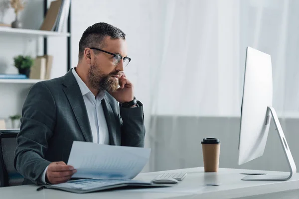 Schöner Geschäftsmann in formeller Kleidung, der mit Smartphone spricht und Dokumente in der Hand hält — Stockfoto