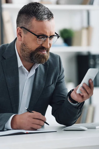 Guapo hombre de negocios en ropa formal celebración de teléfono inteligente y pluma - foto de stock