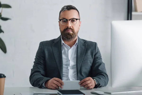 Guapo hombre de negocios en ropa formal sosteniendo el teléfono inteligente y mirando a la cámara - foto de stock