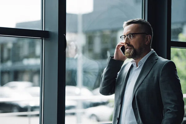 Hombre de negocios guapo en ropa formal y gafas hablando en el teléfono inteligente - foto de stock