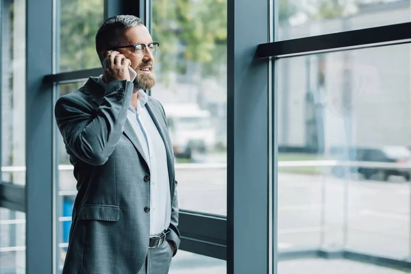 Hombre de negocios guapo en ropa formal y gafas hablando en el teléfono inteligente - foto de stock