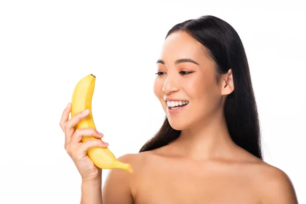 Hermosa sonriente mujer asiática desnuda mirando plátano aislado en blanco - foto de stock