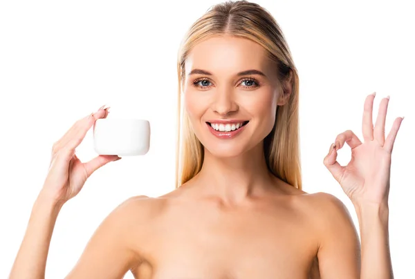 Sonriente mujer desnuda sosteniendo crema cosmética y mostrando ok signo aislado en blanco - foto de stock