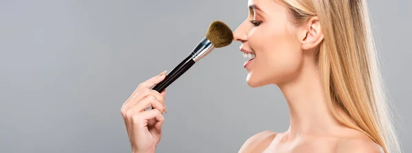 Side view of smiling young naked woman with cosmetic brush isolated on grey, panoramic shot — Stock Photo