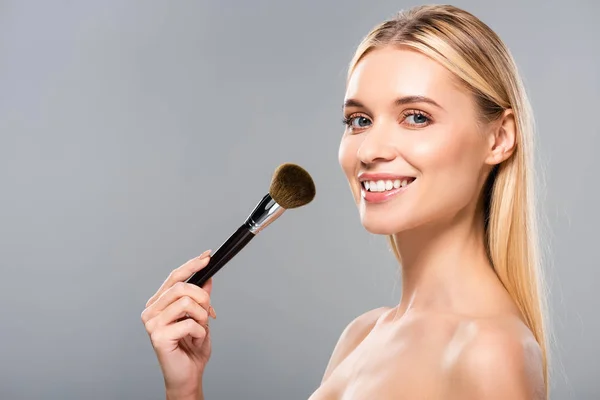 Vista lateral de mulher nua sorridente com escova cosmética isolada em cinza — Fotografia de Stock
