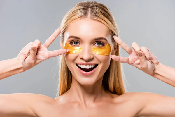 Happy naked blonde young woman with eye patches showing peace signs isolated on grey — Stock Photo