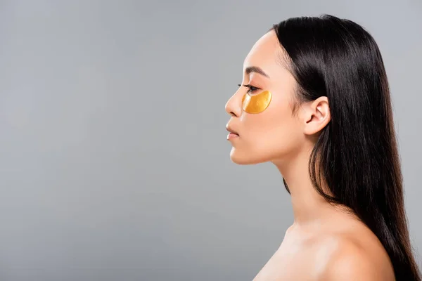 Vista lateral da mulher asiática nua com manchas oculares no rosto isolado no cinza — Fotografia de Stock